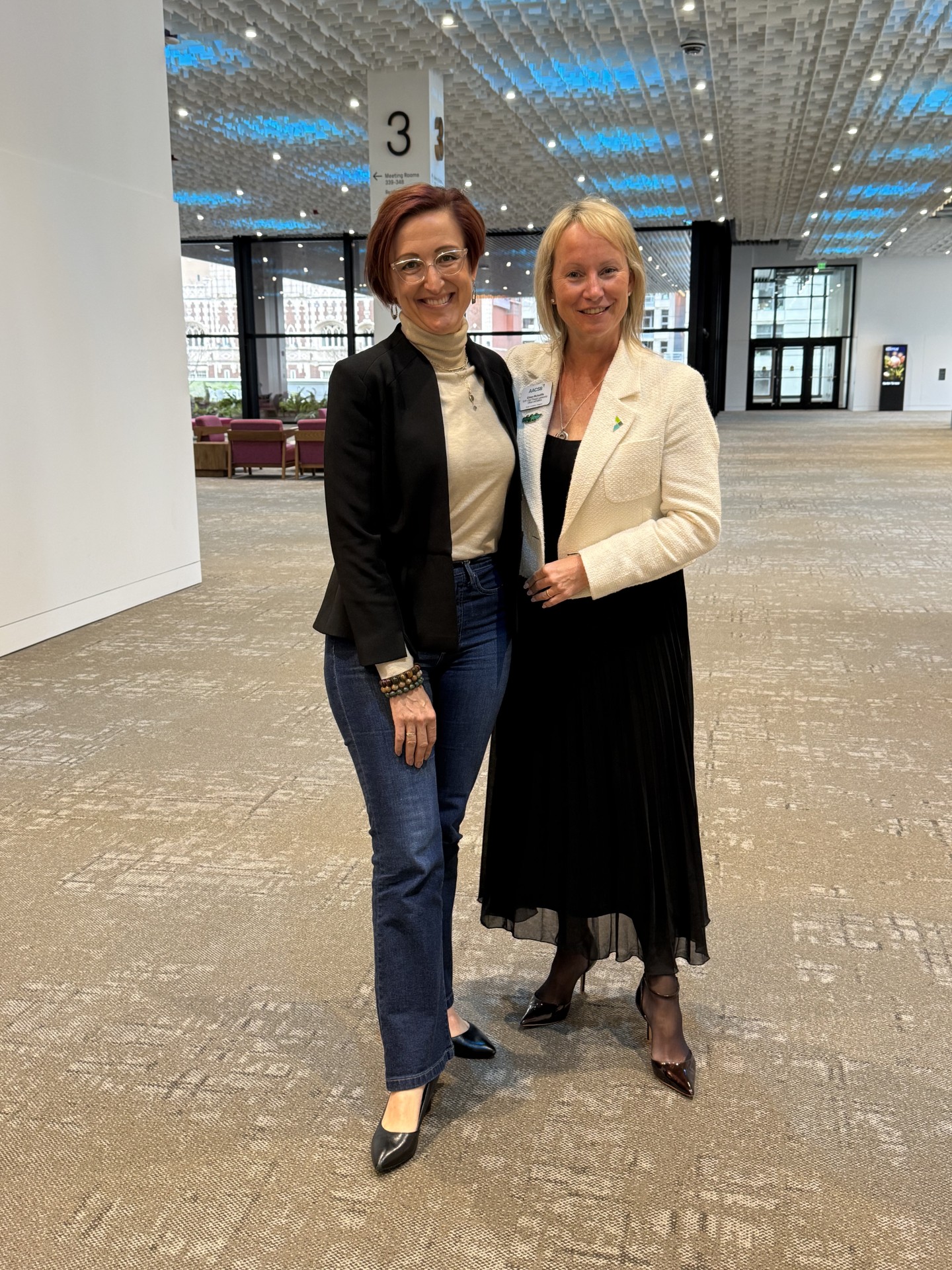 Julia Minson and Eileen McAuliffe posing together, standing in a Seattle Convention Center Summit Building hallway