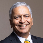 Ajay Vinze of George Mason University with black blazer, white collared shirt, and gold tie with diagonal dark blue stripes, silver side-parted hair, dark eyes, wide smile, and olive complexion